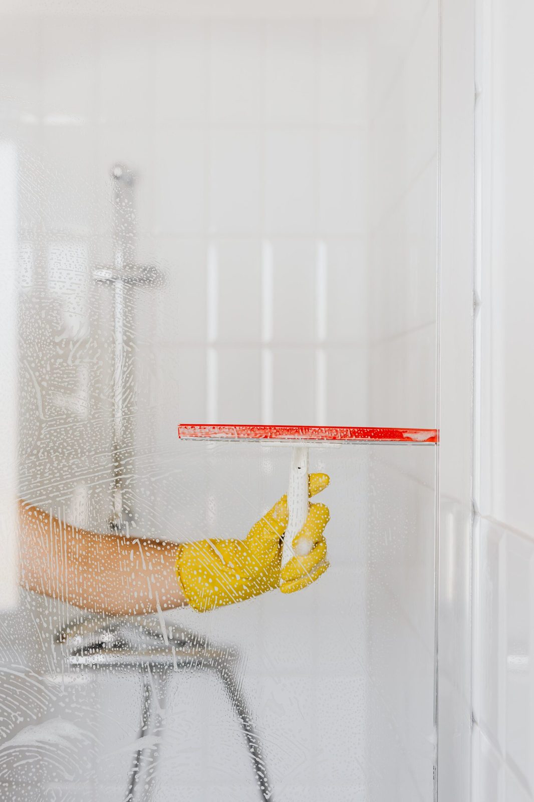 Bright bathroom shower being squeegeed by a cleaner in yellow gloves